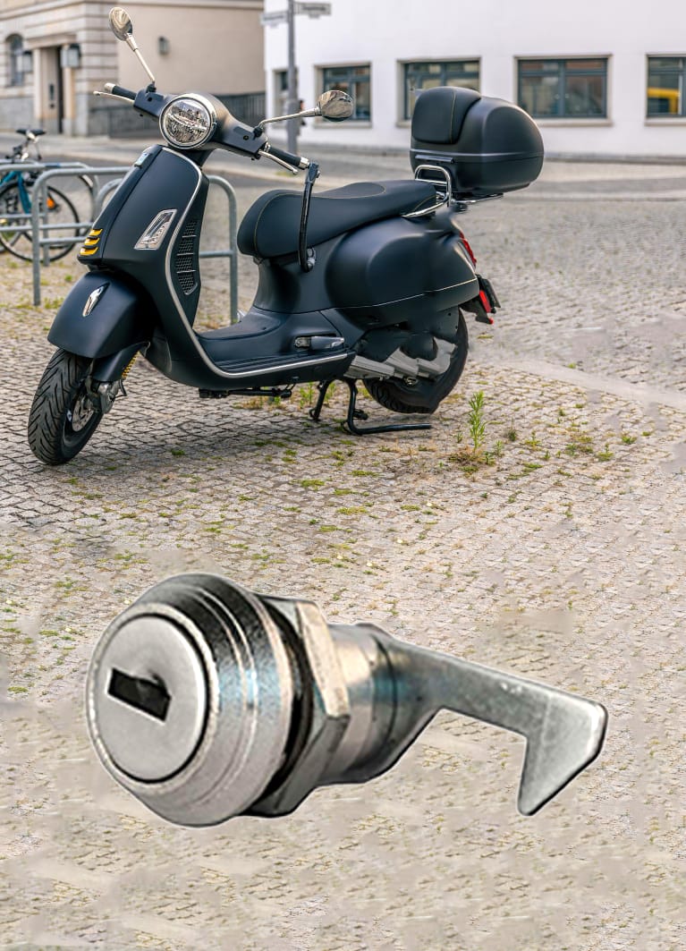 Immagine di uno scooter con bauletto e della serratura con camma a gancio che ne protegge il contenuto Immagine di uno scooter con bauletto e della serratura con camma a gancio che ne protegge il contenuto